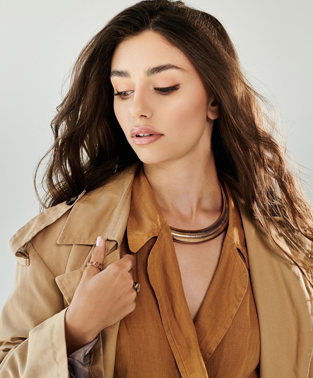 Woman in stylish outfit with jewelry, soft expression.