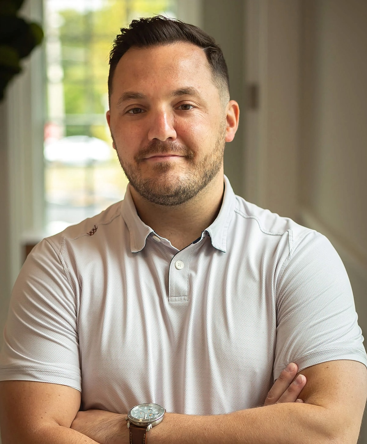 Man in polo shirt with arms crossed, smiling.